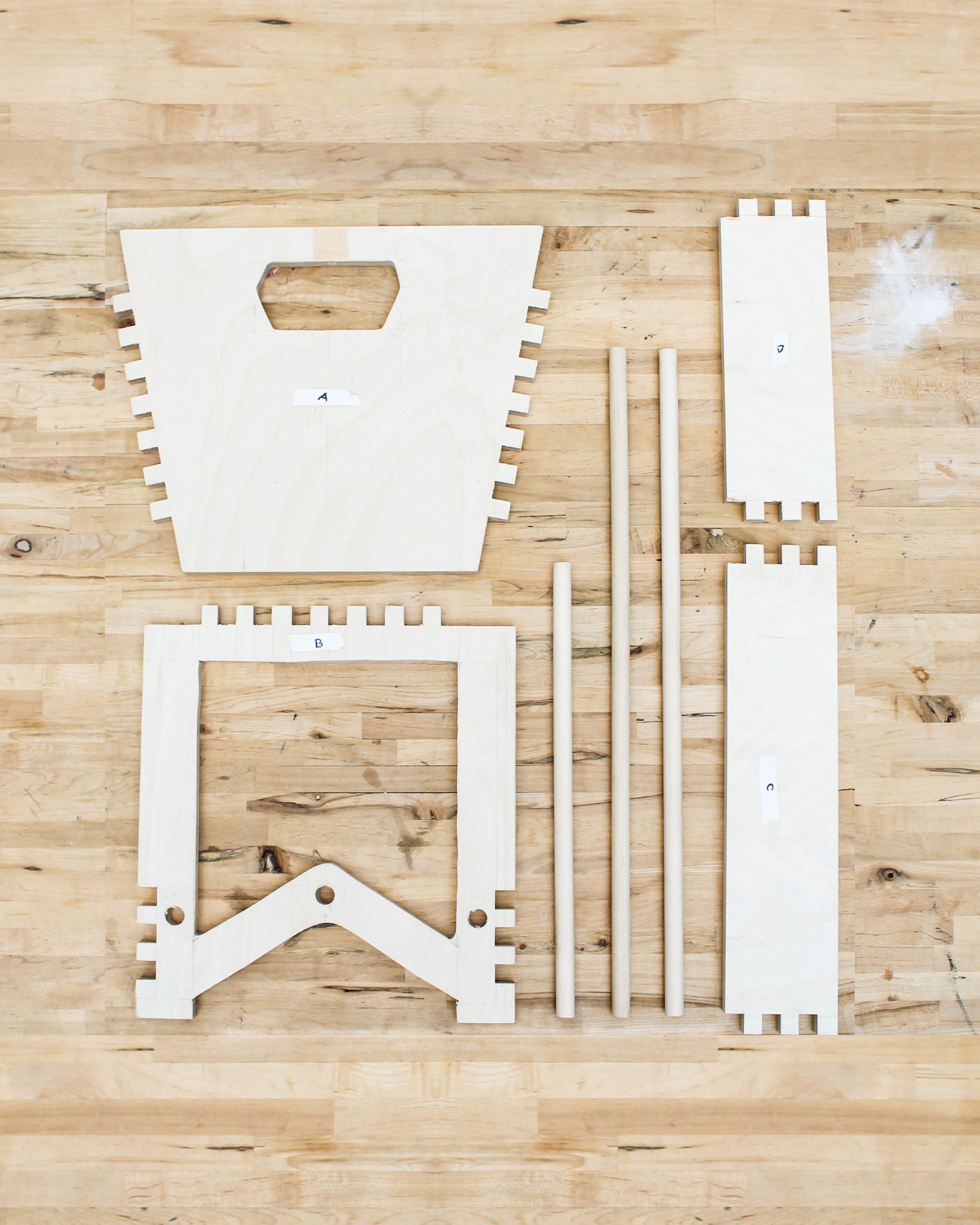 Disassembled wooden parts and dowels for a piece of furniture or structure, laid out on a wooden floor, labeled with letters A, B, and C.