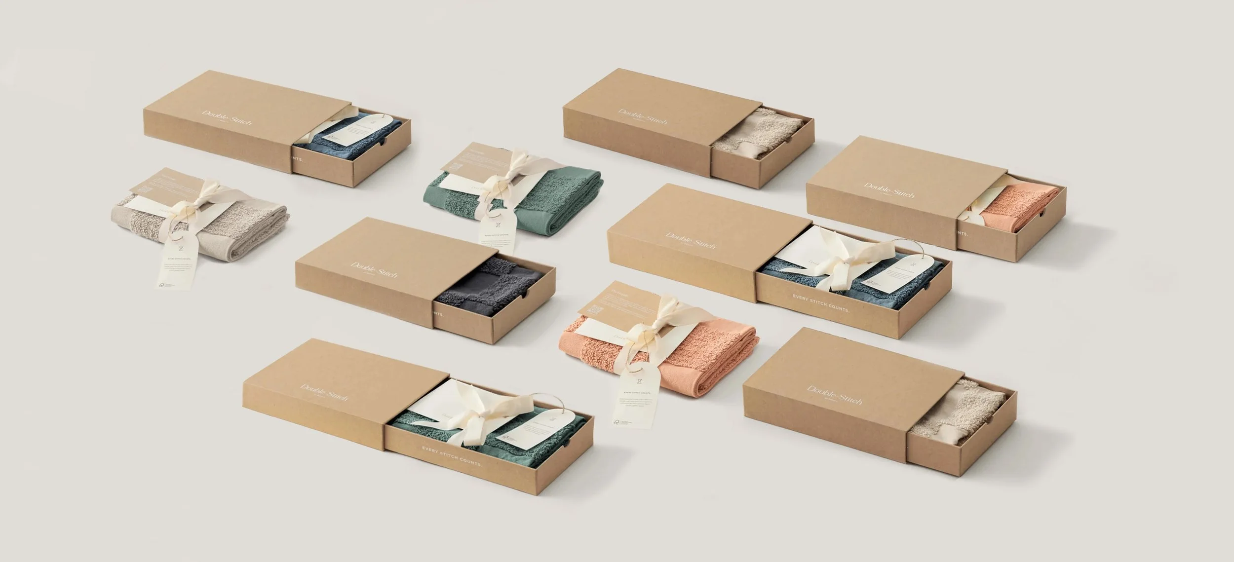 Collection of neatly folded towels in beige, green, peach, gray, and navy blue, each wrapped with a cream ribbon and placed in minimalist cardboard boxes on a white background.