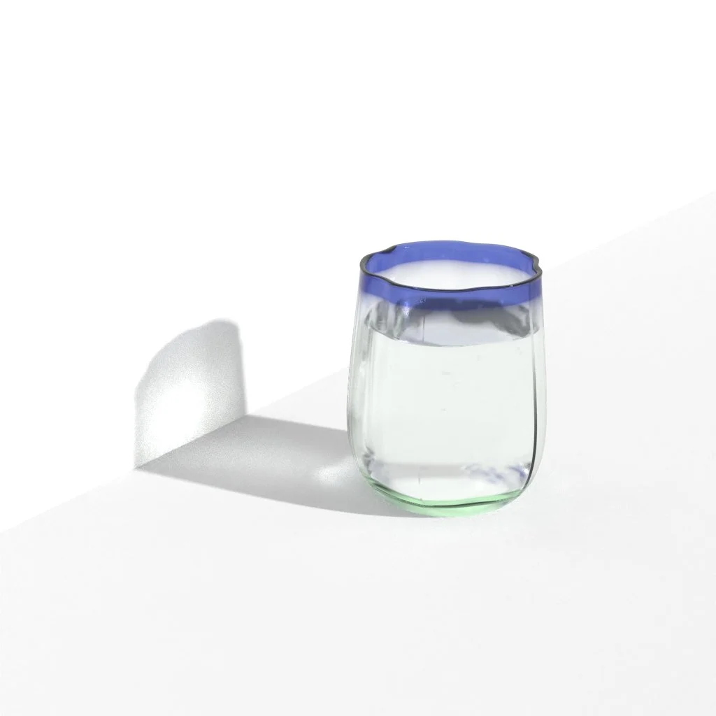 A glass of water with a blue rim, casting a shadow on a white surface.