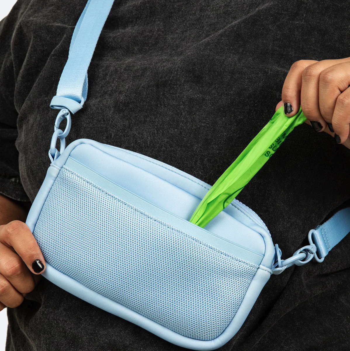 Person wearing a black shirt with a light blue crossbody bag, placing a green item into the bag.  Lucy & Co. Crossbody treat bag.