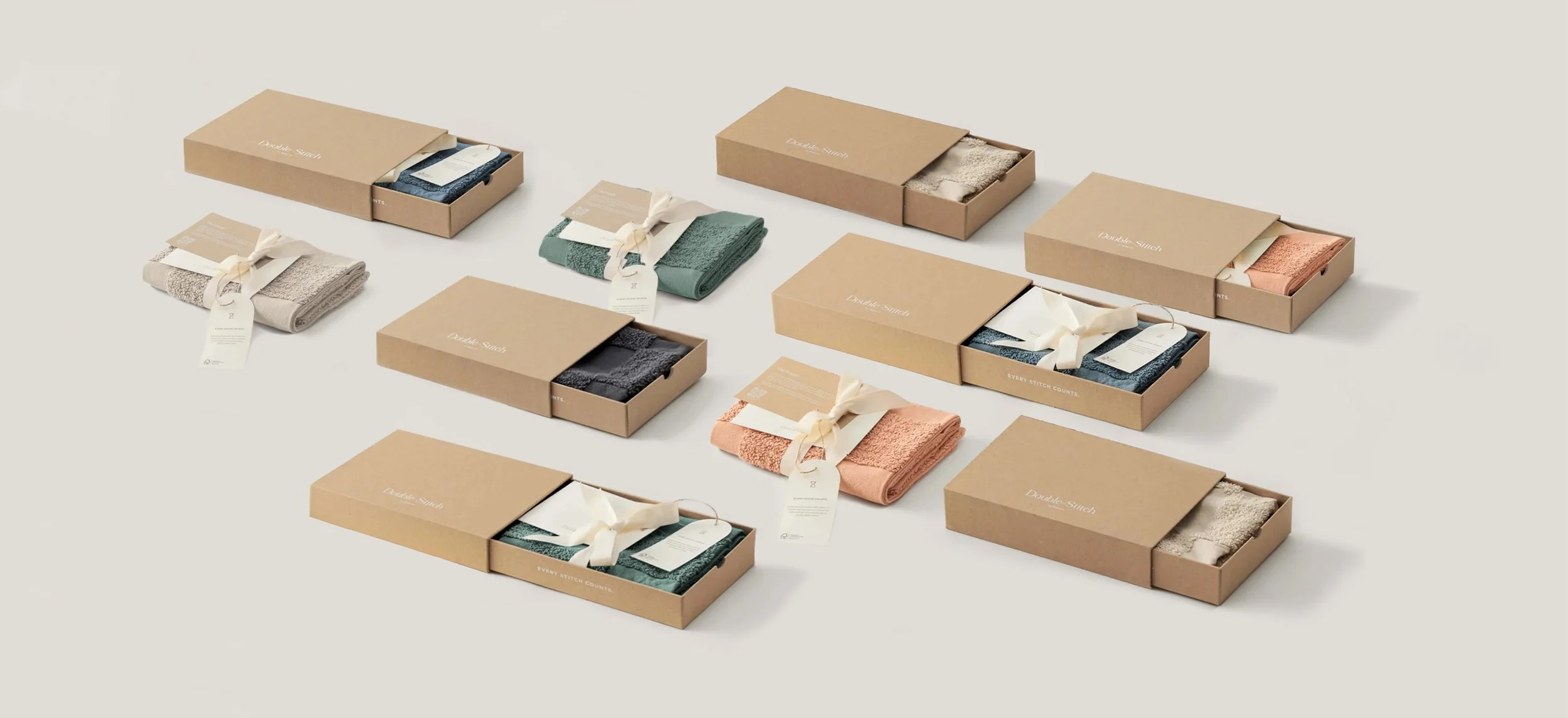 Multiple sets of neatly folded towels in pastel colors, each wrapped with a ribbon and placed inside beige boxes on a light background.