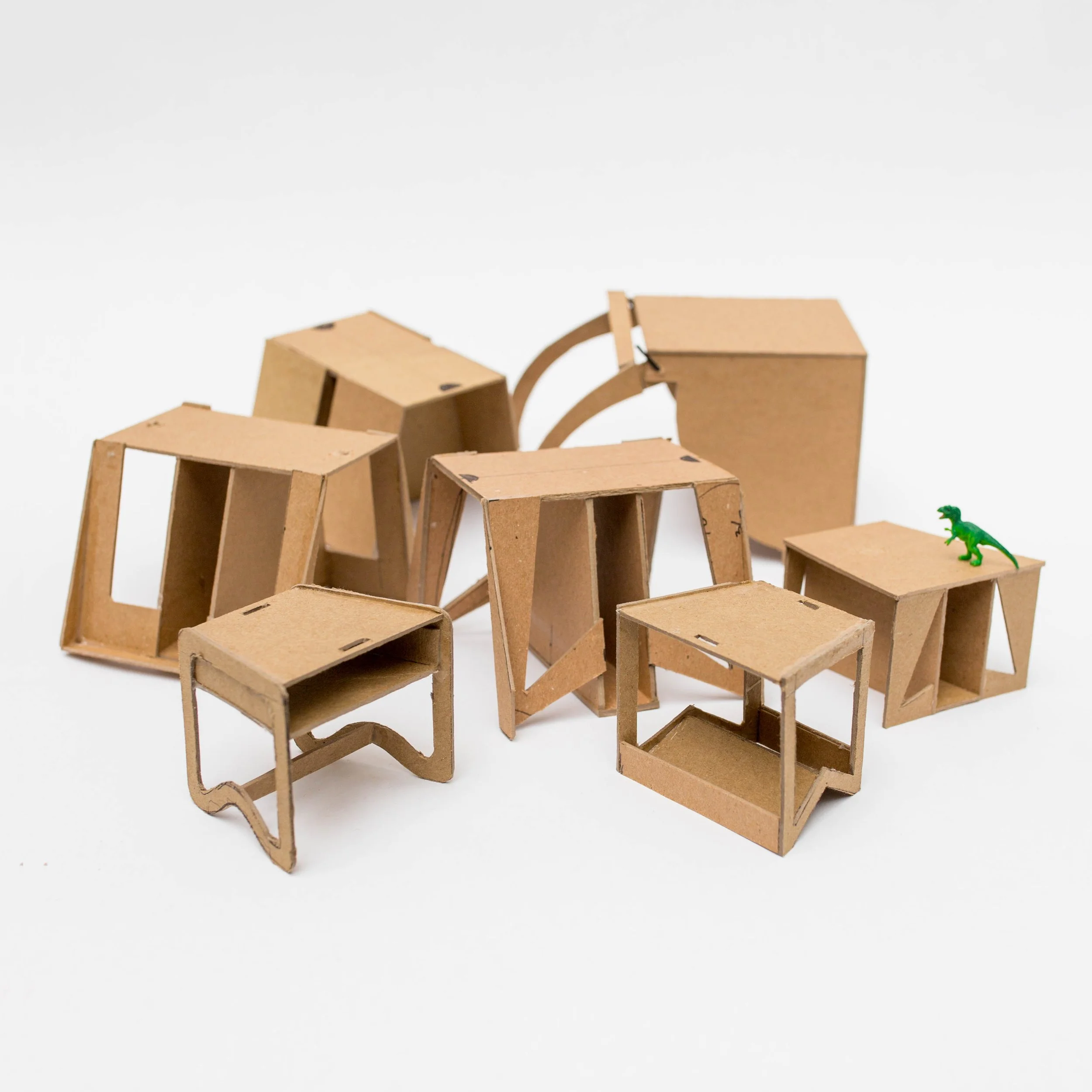 Collection of small cardboard furniture pieces and a green dinosaur figurine on a plain white background.