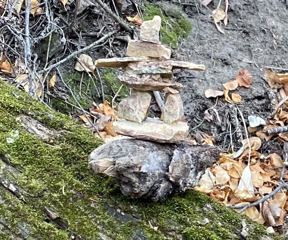 Stone Inukshuk resting on a moss-covered log, symbolizing integration and the process of becoming more fully ourselves.