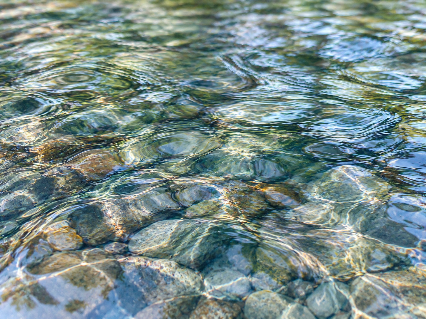 Clear rippling water revealing stones beneath the surface, symbolizing the unconscious patterns and deeper layers of experience explored in Jungian and depth psychology.