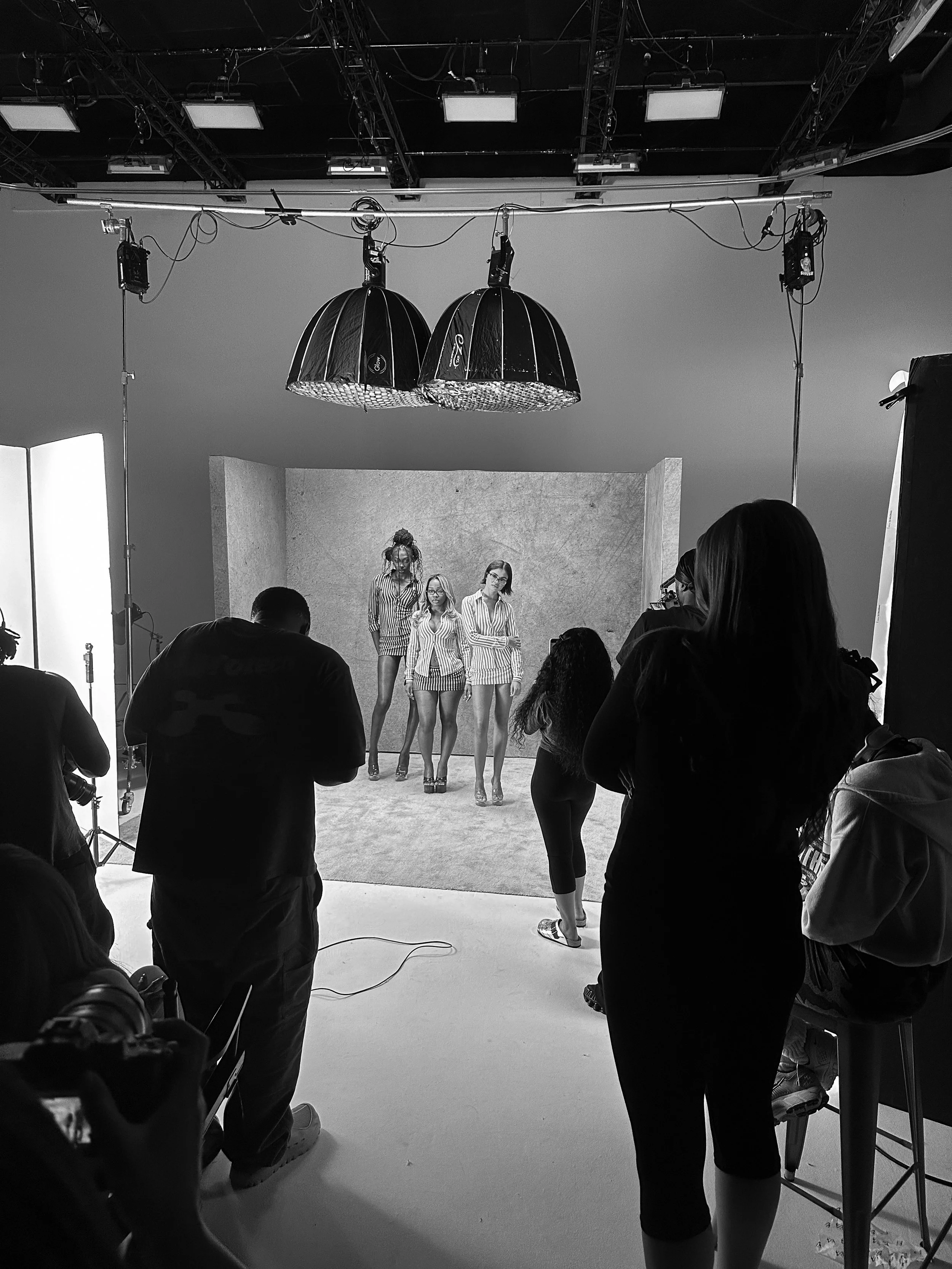 Women models in striped outfits posing in a photo studio with photographers and crew around, black and white image.