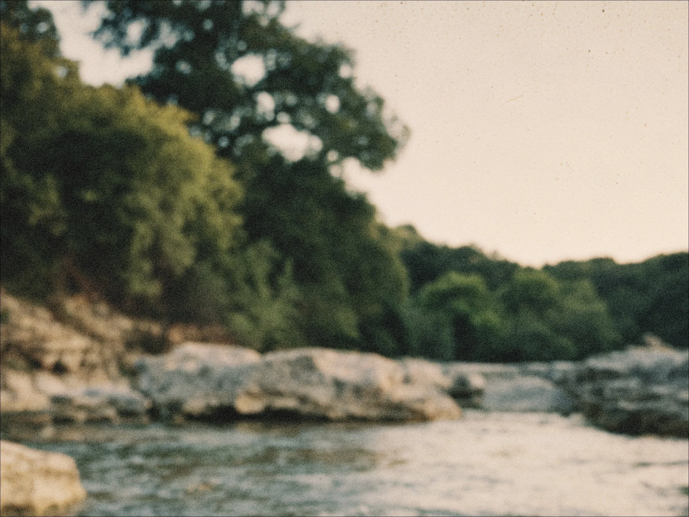 A blurred outdoor scene of a river with rocks and green trees along the banks.