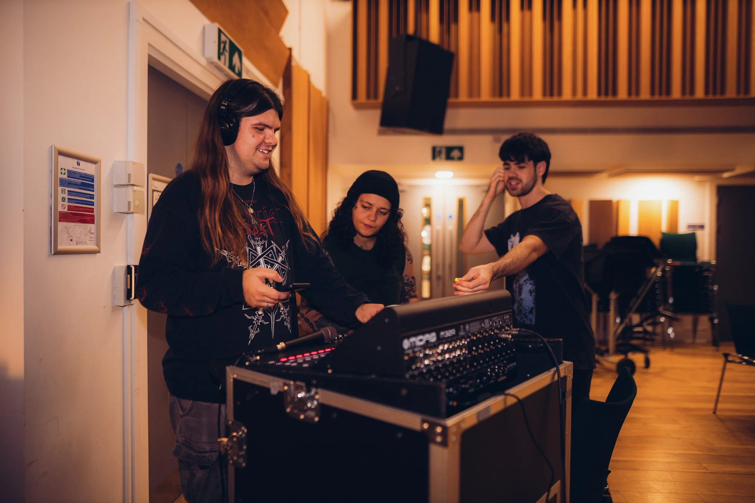 Ben in a hall stood at a mixing desk with two musicians beside him