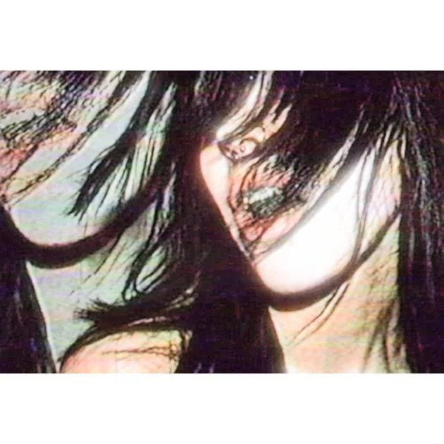 Close-up of a woman with long, dark hair partially covering her face, with some strands falling across her eyes.