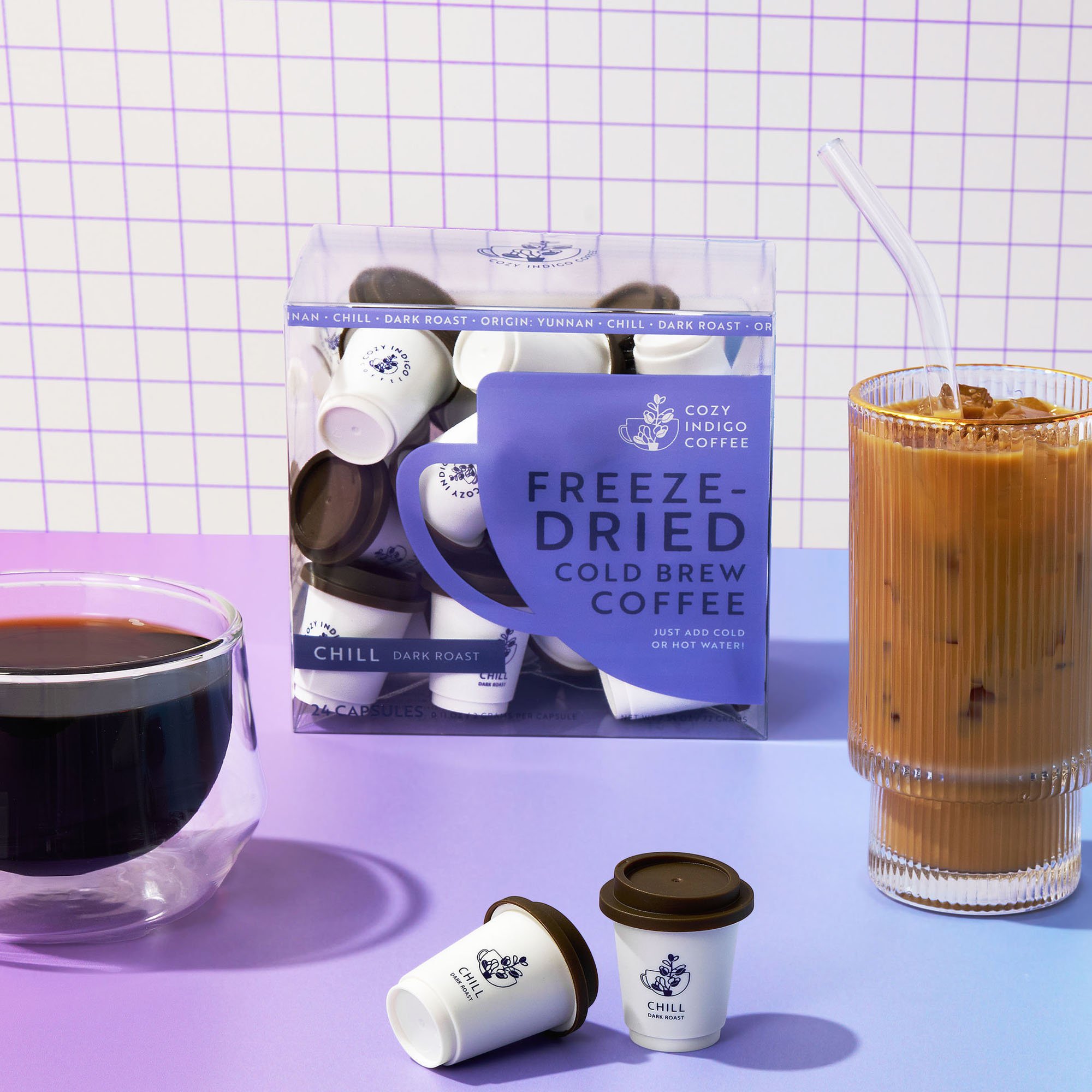 A box of CHILL freeze-dried coffee capsules beside a glass of iced coffee and a cup of black coffee on a pastel purple table.