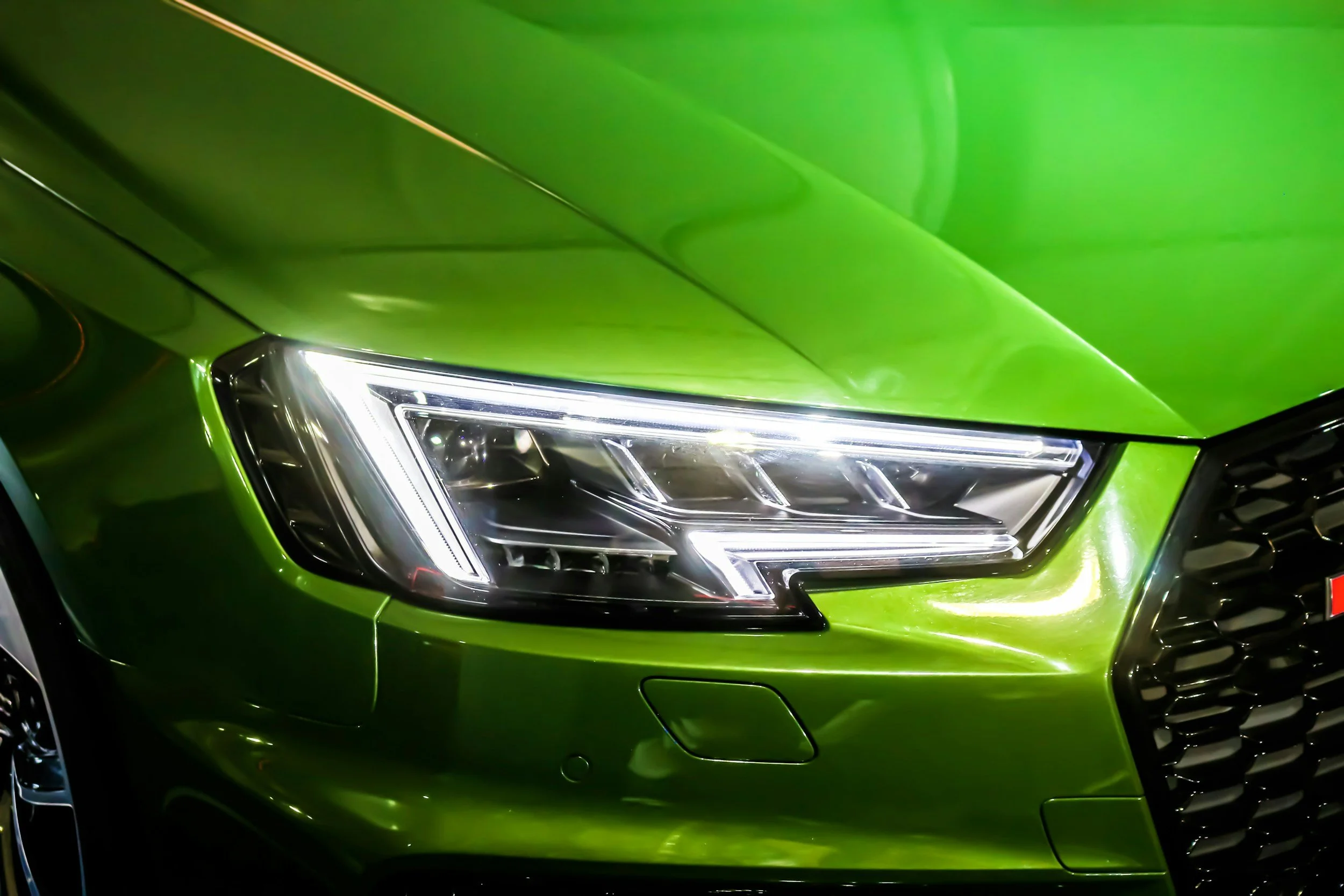 Close-up of a green car's front left side, showing the headlight and part of the grille.