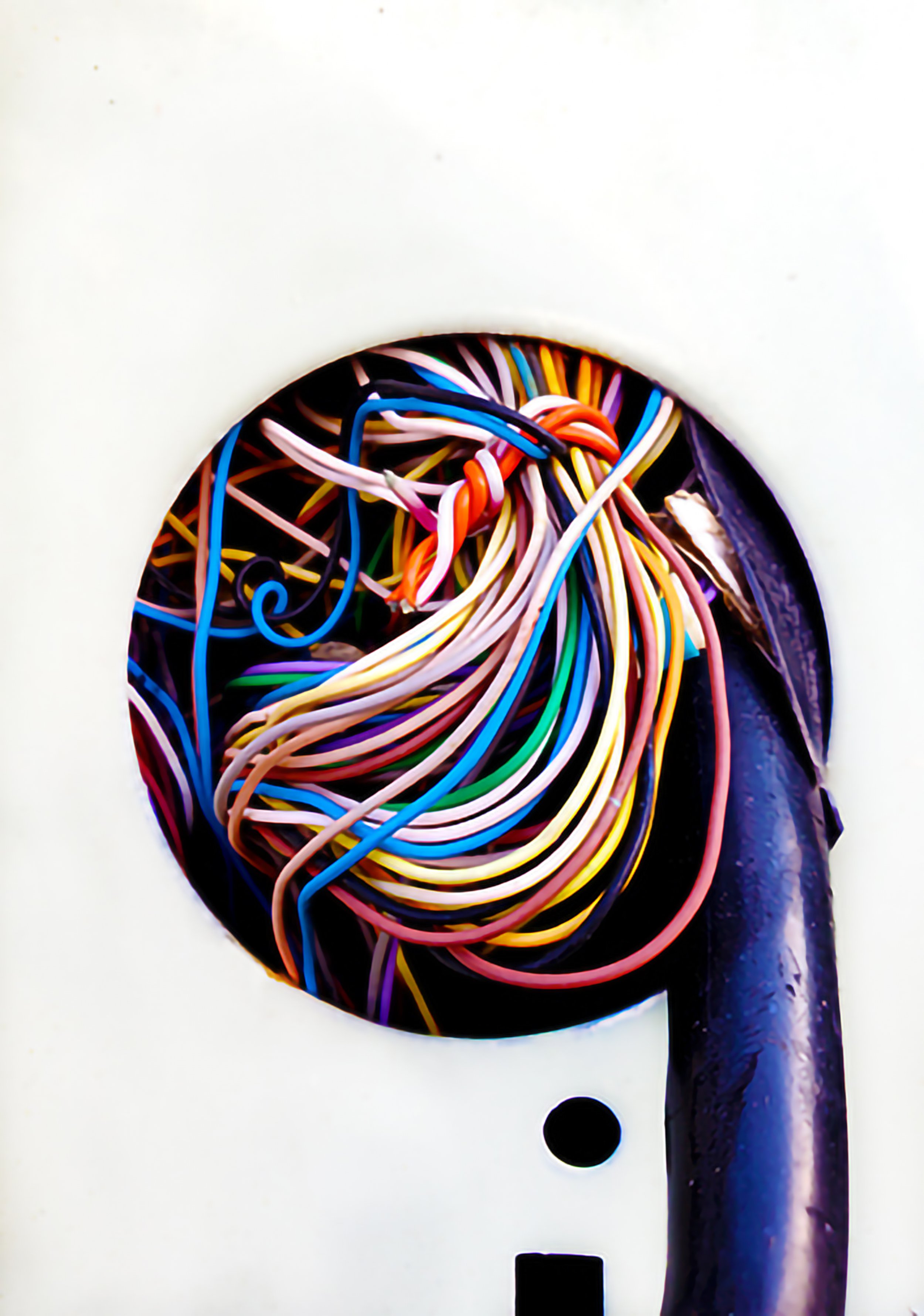 Close-up of a white outdoor electrical box with a circular hole revealing an array of colorful tangled wires and cables inside.