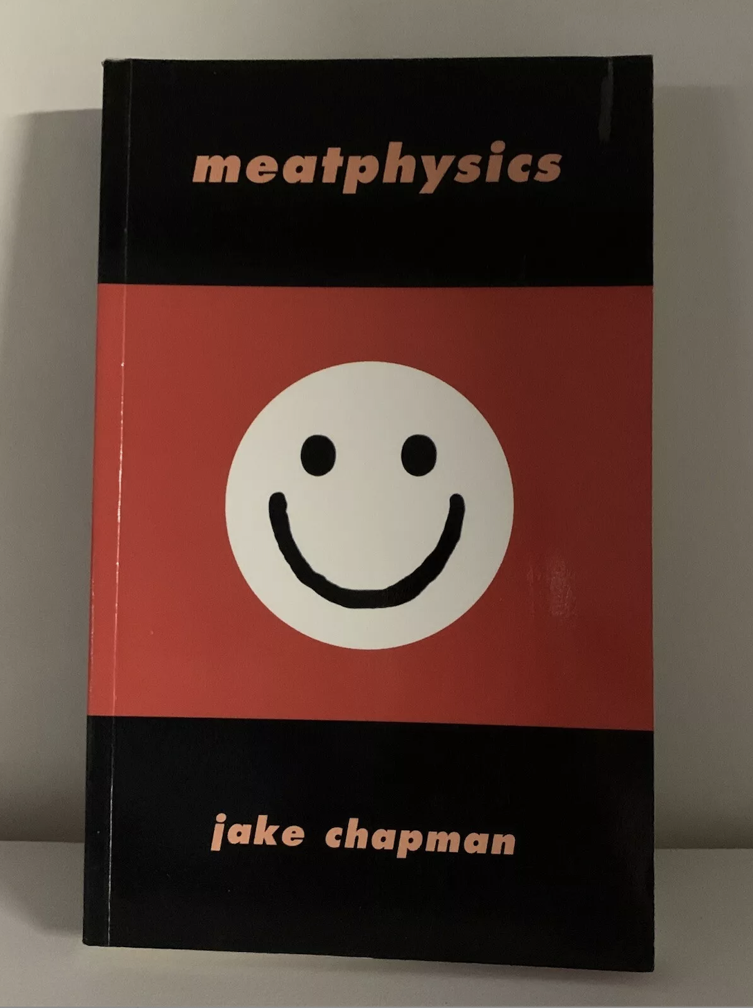 A book titled 'meatphysics' by Jake Chapman with a black and red cover featuring a white smiling face.