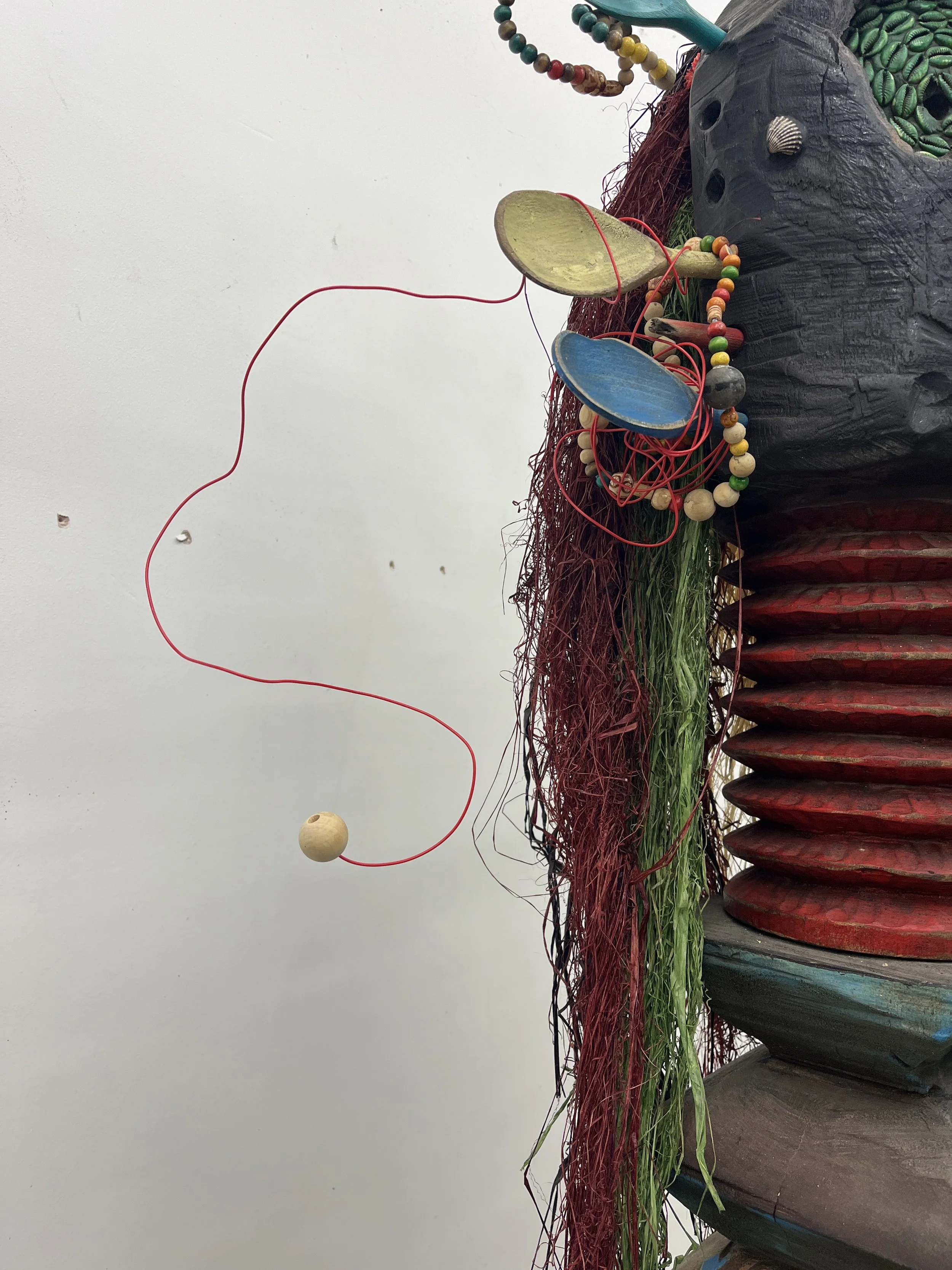 Close-up of a colorful, artistic sculpture featuring metal and wooden elements, with beads, painted surfaces, and textured materials.