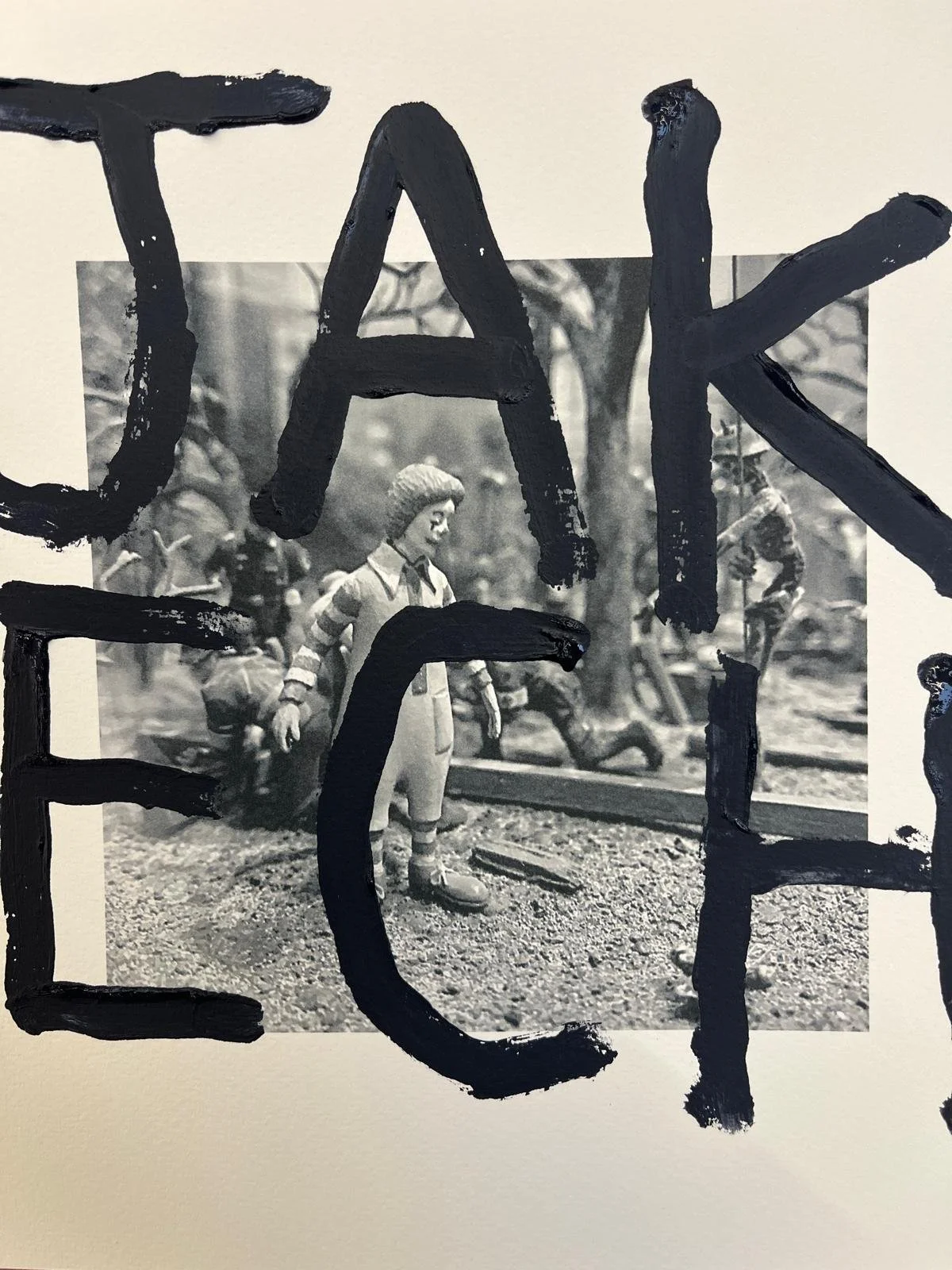 Black and white photo of a small toy soldier figurine standing outdoors on a textured surface, with blurred trees and other figures in the background. Painted black letters overlay the image, spelling out "TAKE."