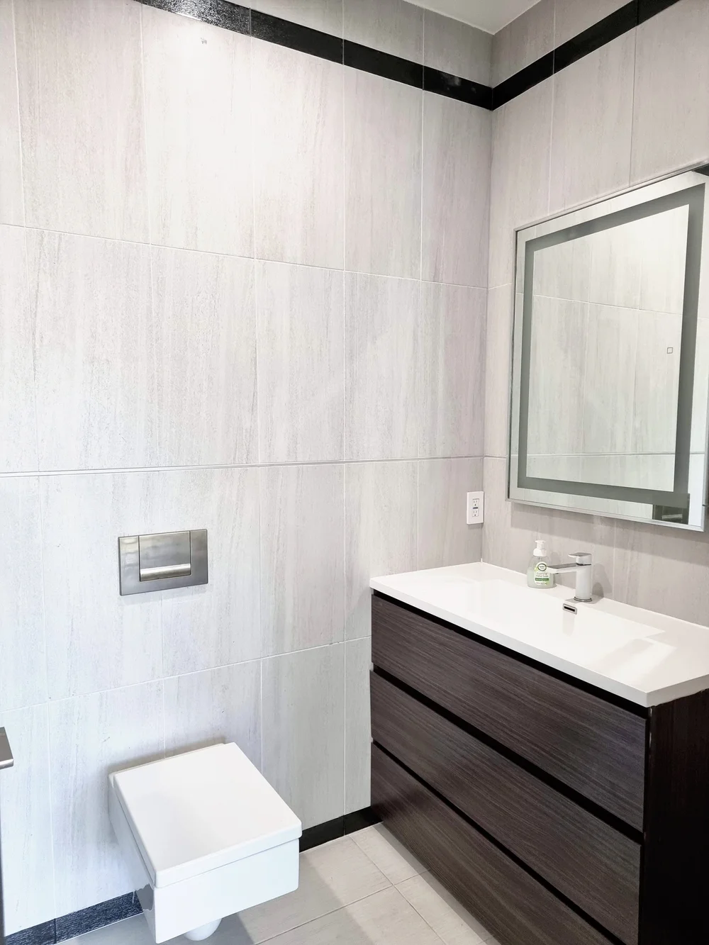 Modern bathroom remodel with large-format wall tile, a floating vanity, a lighted mirror, and a wall-hung toilet