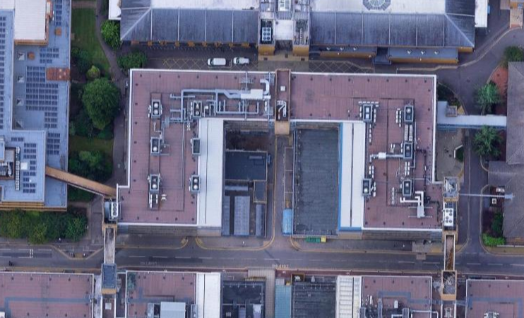 Aerial view of city buildings with rooftops and streets, including some parked cars.