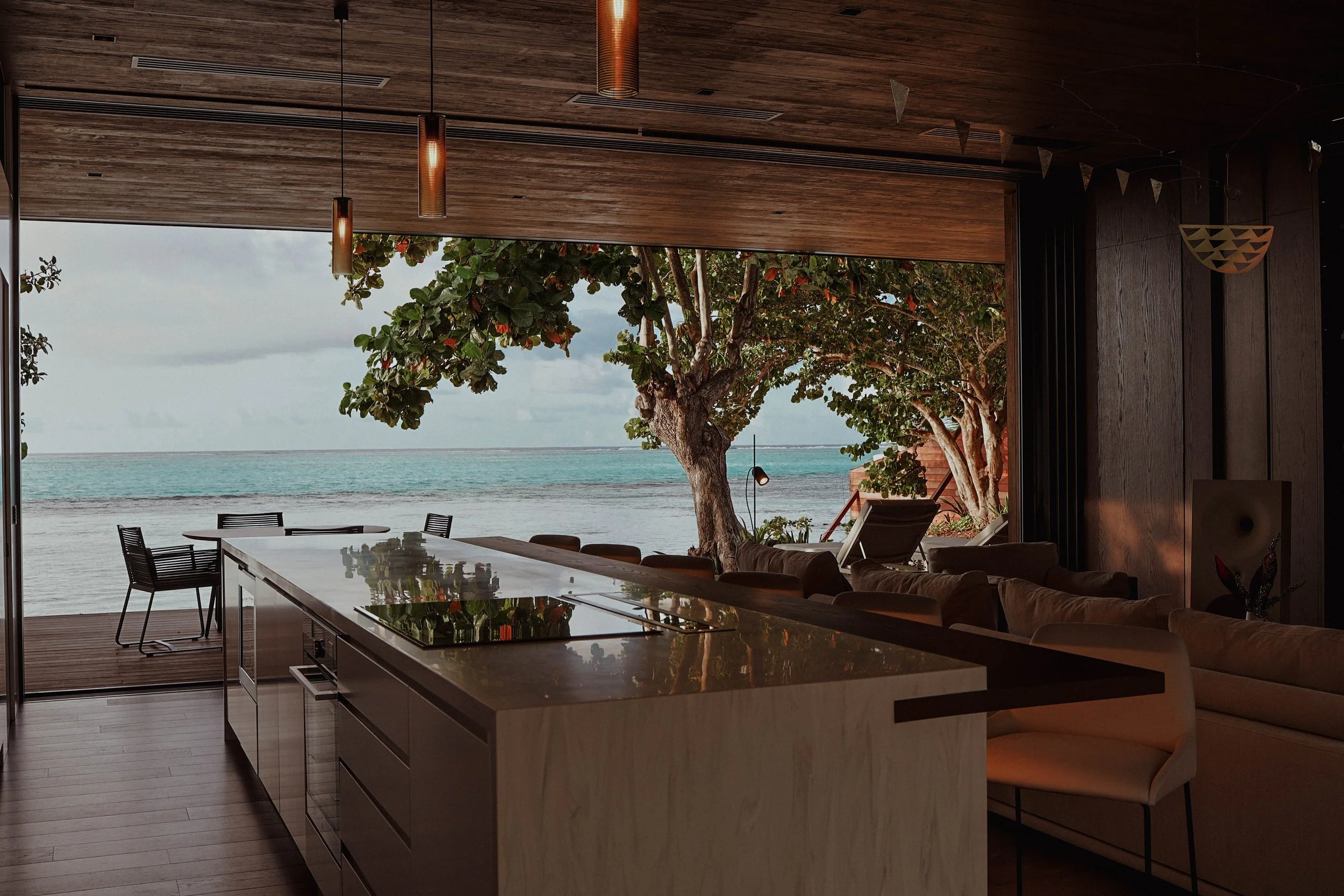 Salon intérieur avec vue sur la plage et la mer, arbres, canapé beige, table de cuisine moderne