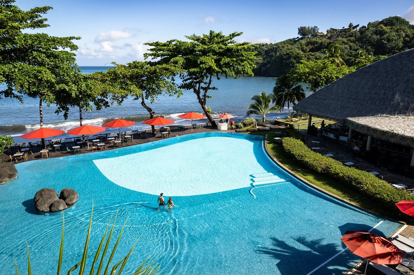 Piscine à débordement dans un Resort bord de mer Moorea  avec des parasols, des palmiers, et une plage avec de la mer en arrière-plan