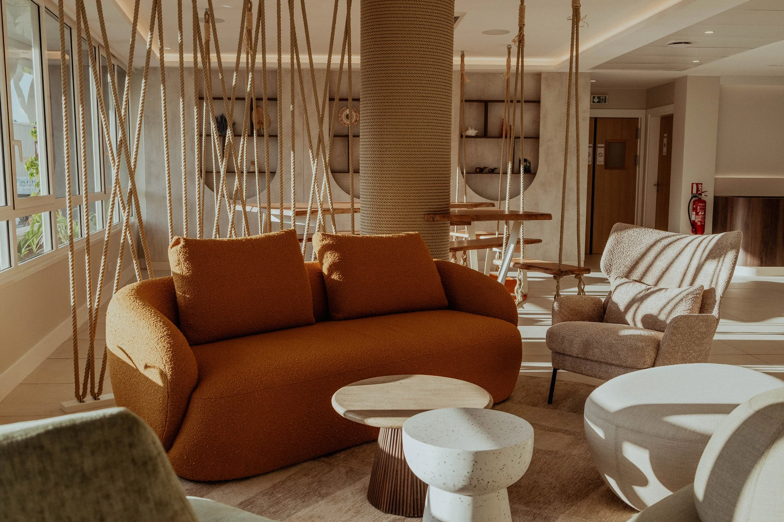 Un salon avec un canapé orange, un fauteuil beige, et deux tables basses en bois et en pierre, dans un espace lumineux avec une décoration moderne.