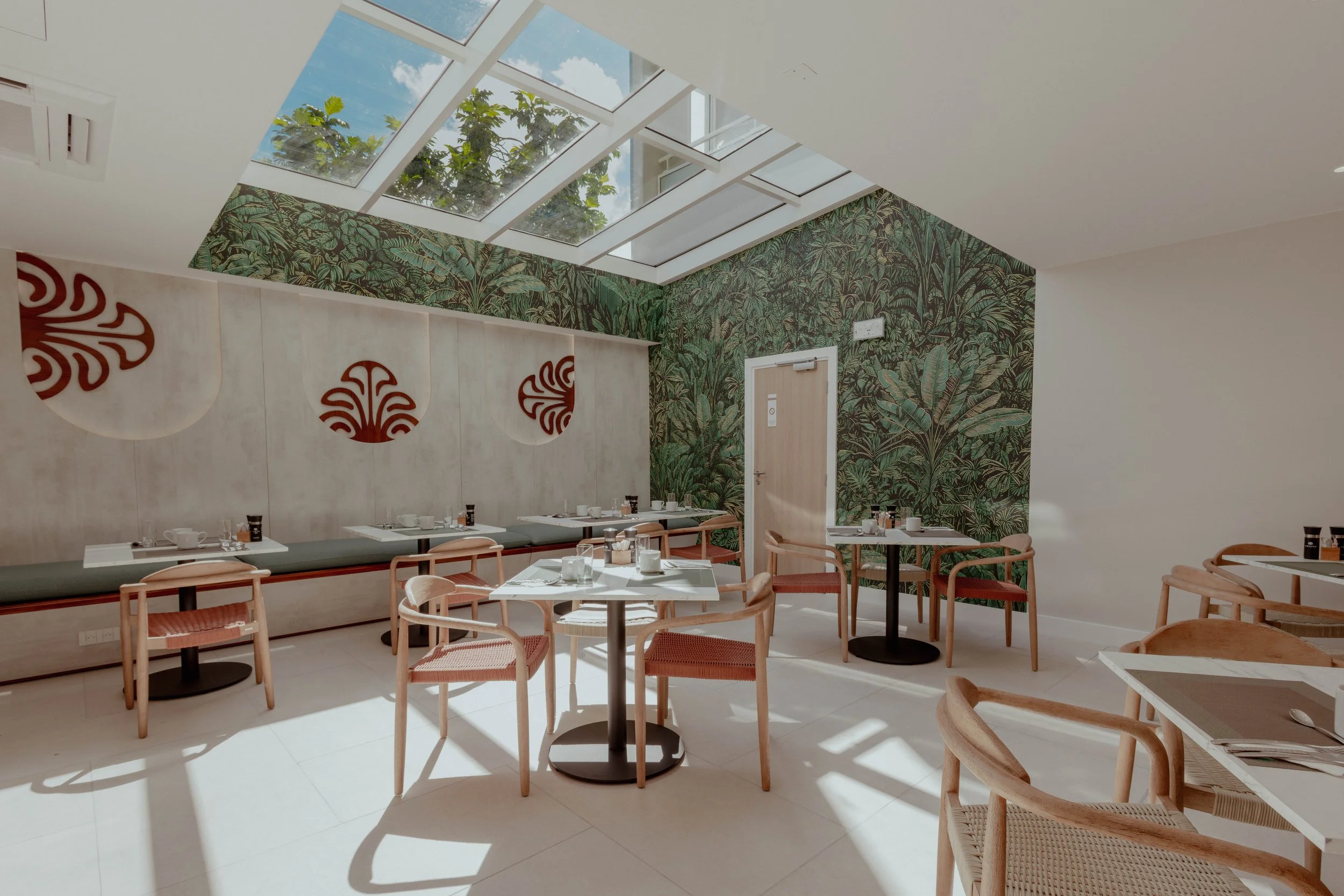 Salle à manger lumineuse avec des tables et des chaises en bois, un mur végétal et un plafond en verre laissant entrer la lumière naturelle.