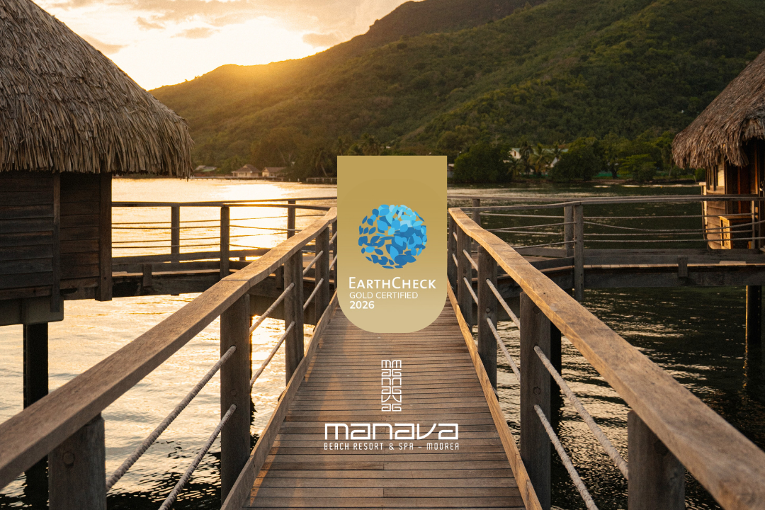 Jetée en bois menant à un bungalow en chaume face à un lac au coucher du soleil, avec des montagnes verdoyantes en arrière-plan, logo d'EarthCheck, certification or 2026, et mention de Manava Beach Resort & Spa Moorea.