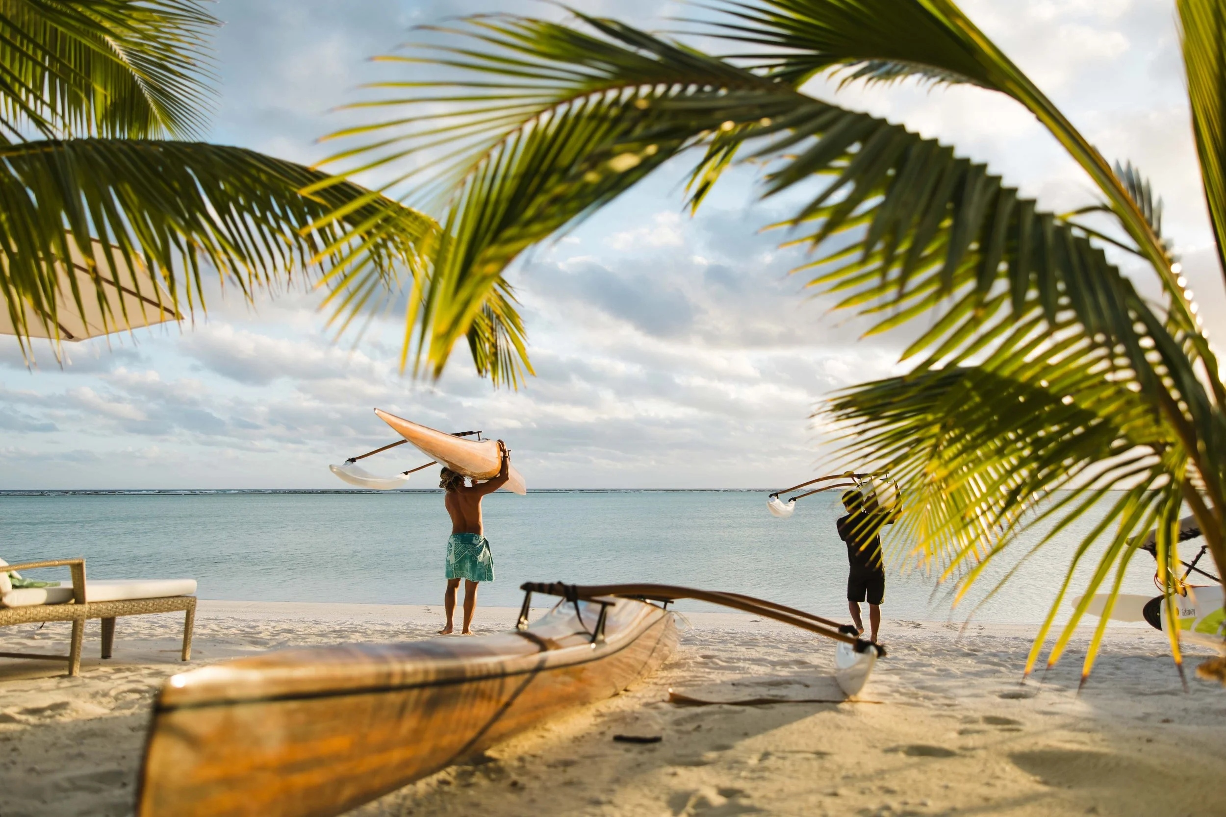 Plage avec deux personnes préparant des kayaks, vue sur la mer, entourée de palmiers.