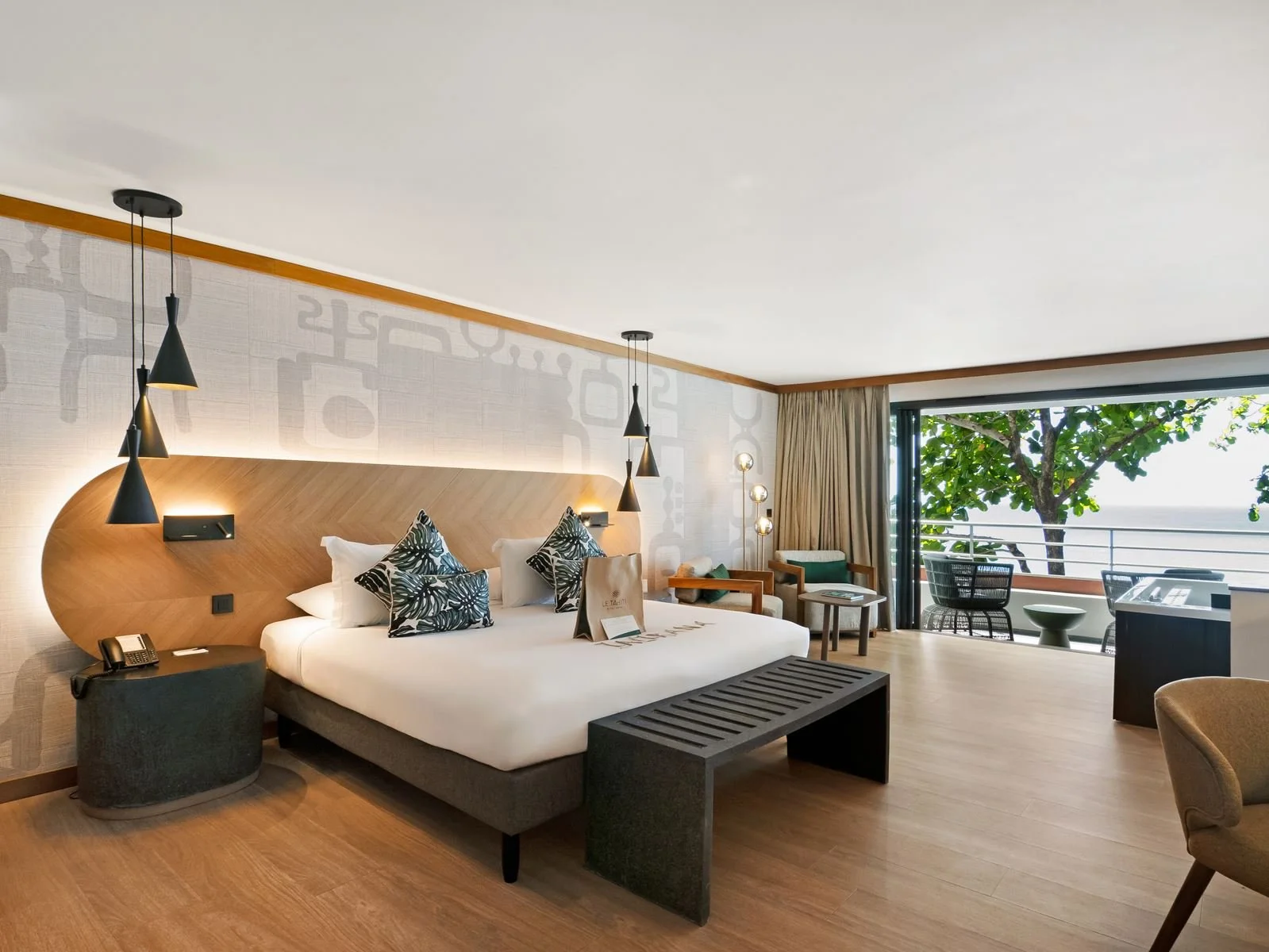 Chambre d'hôtel avec lit, fauteuils, terrasse avec vue sur la mer, et décoration moderne.
