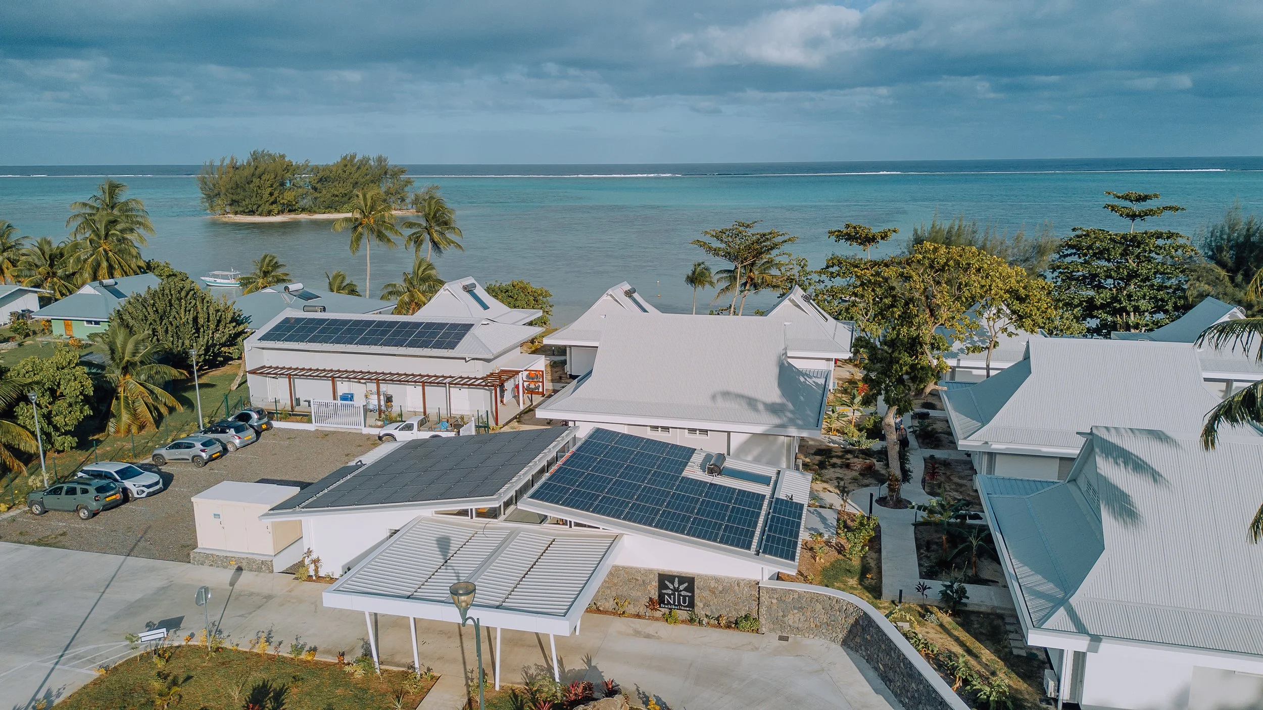 Villas blanches avec toits en métal blanc et panneaux solaires, face à la mer avec des palmiers et un littoral rocheux