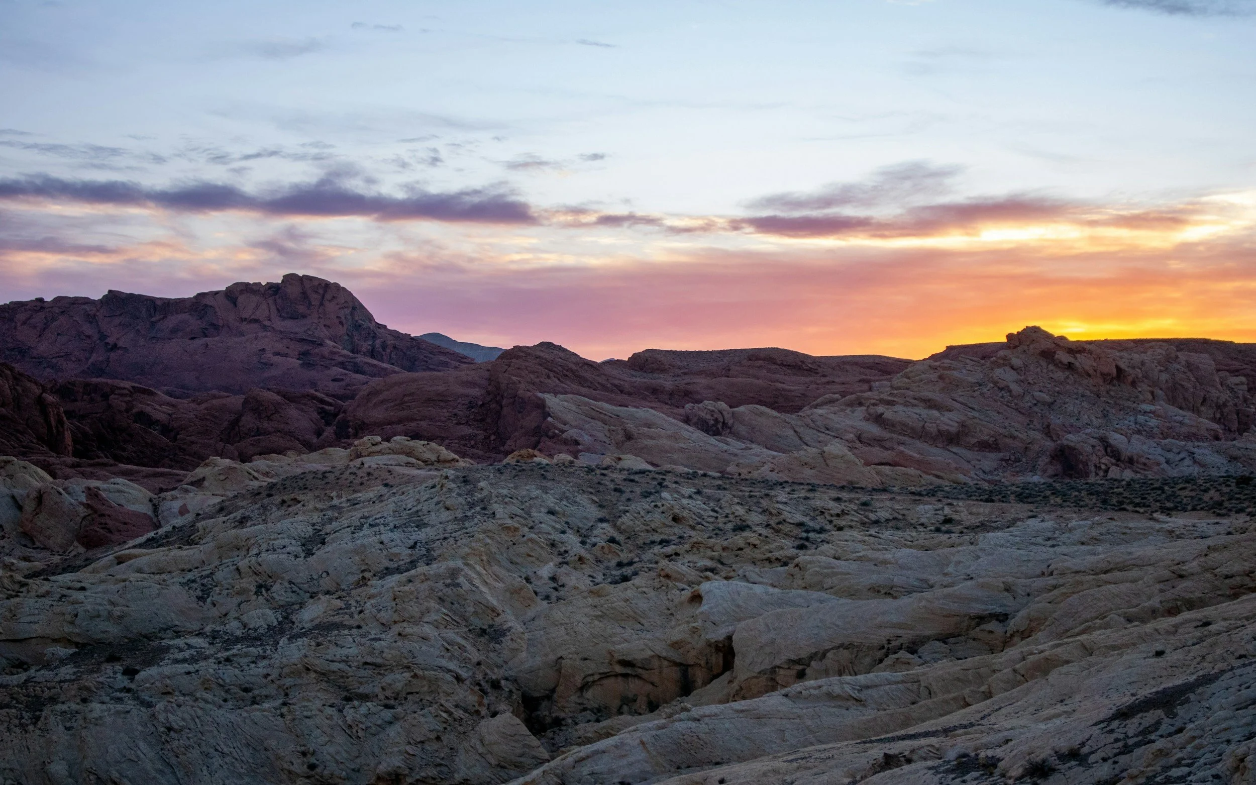 Desert landscape during sunset with rocky formations and a sky with scattered clouds.