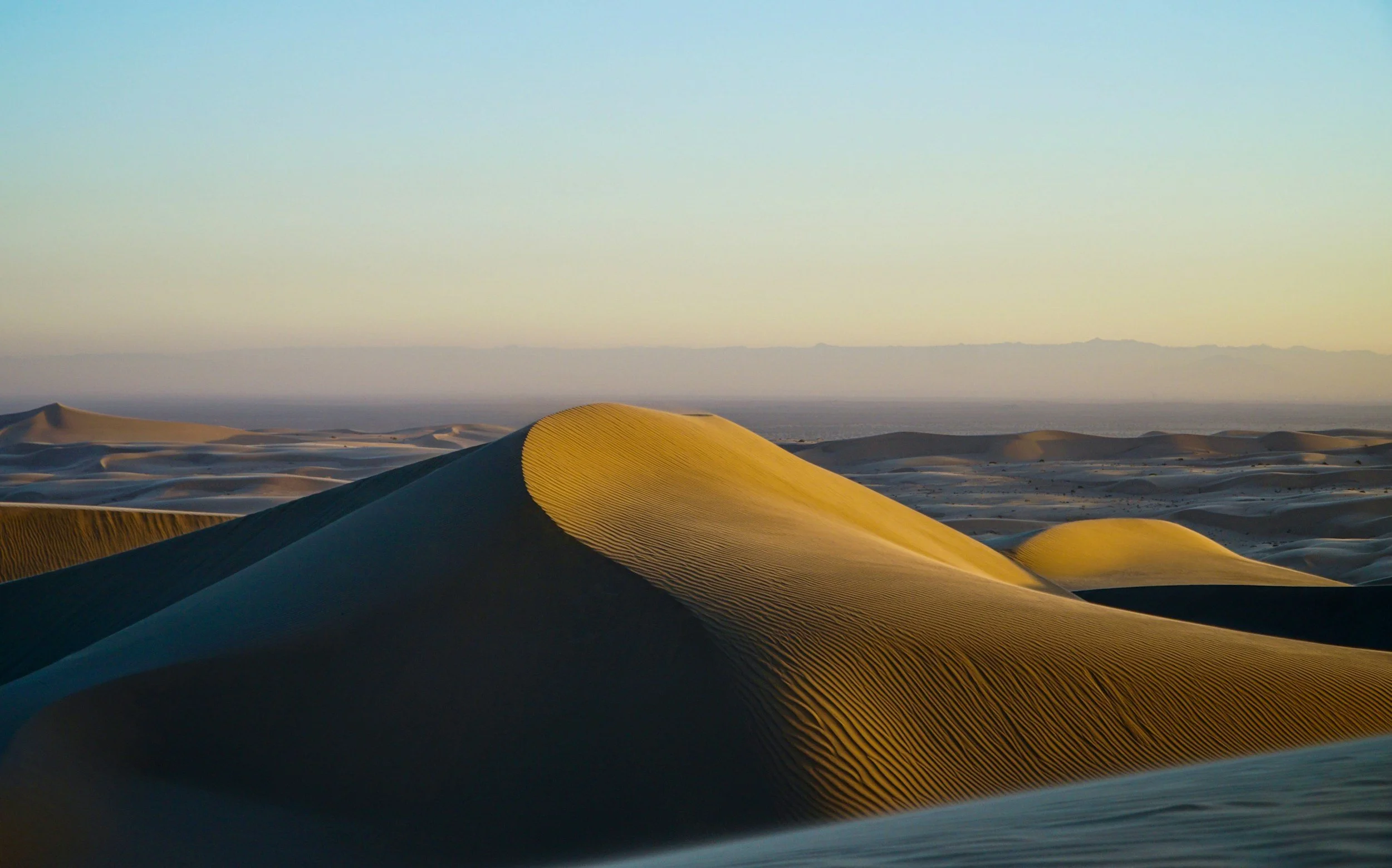 Dunes in a desert at sunset with clear sky.