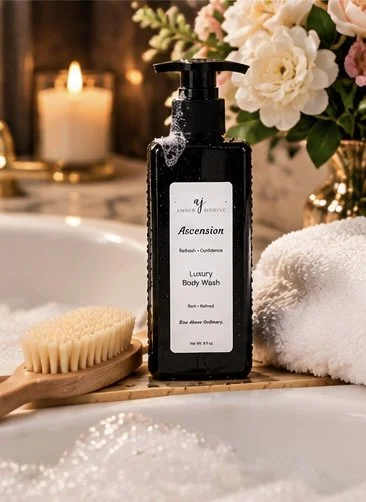 Ascension Luxury Body Wash in a black 8 oz pump bottle displayed beside a bubble bath with soft white towels, a body brush, fresh flowers, and warm candlelight.
