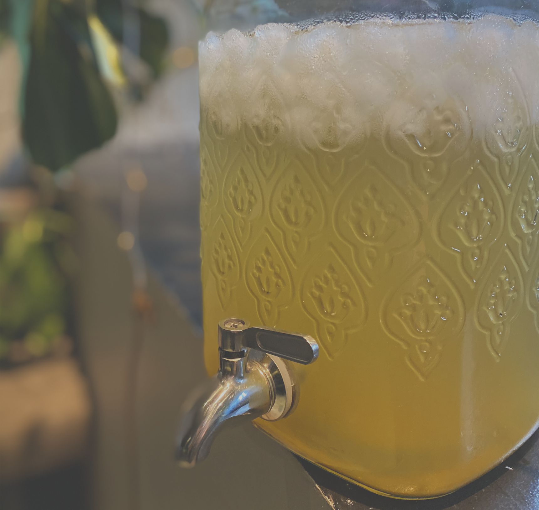 Ein Glas mit gelbem Getränk, das eine dekorative Außenstruktur hat, darunter eine kleine Metallarmatur