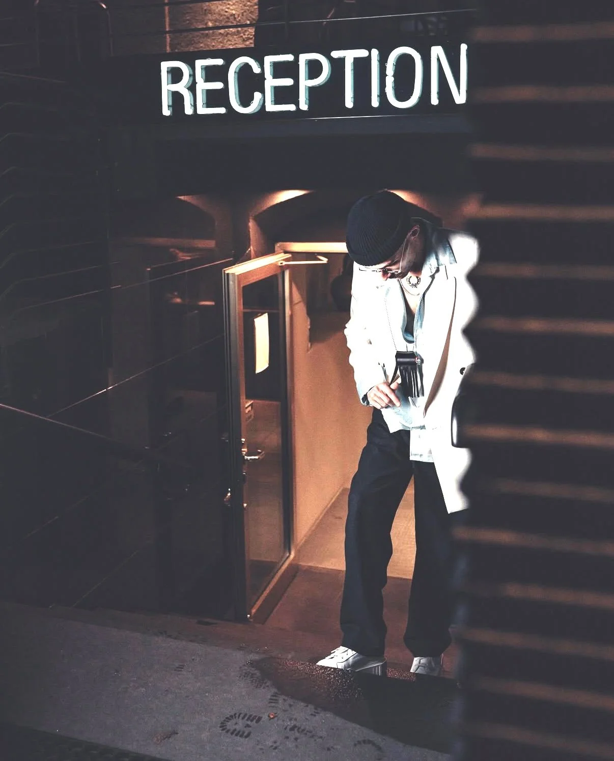 Junge Person, die an einem Empfangsschalter steht, trägt eine weiße Jacke, eine schwarze Mütze und liest eine Eintrittskarte.