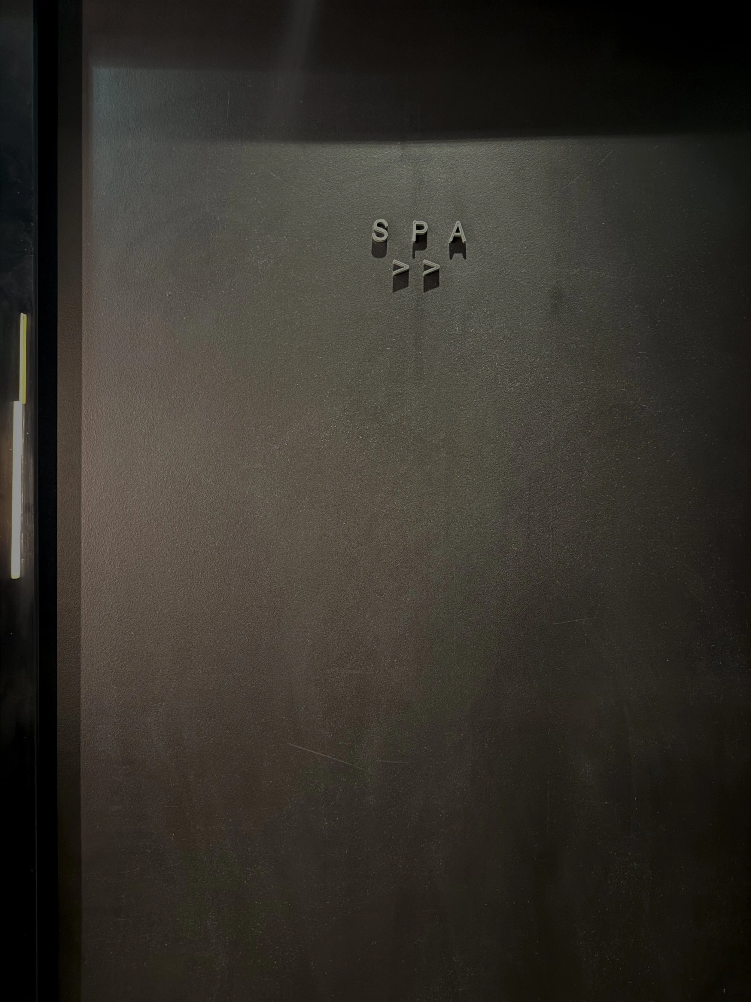 Schwarze Tür mit silbernen Buchstaben und Symbolen, die den Spa-Bereich anzeigen.