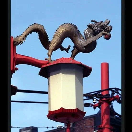 A dragon sculpture on a light fixture attached to a pole against a blue sky, with electrical wires nearby.