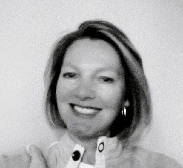 Black and white photo of a smiling woman with shoulder-length hair wearing a light-colored top and earrings.
