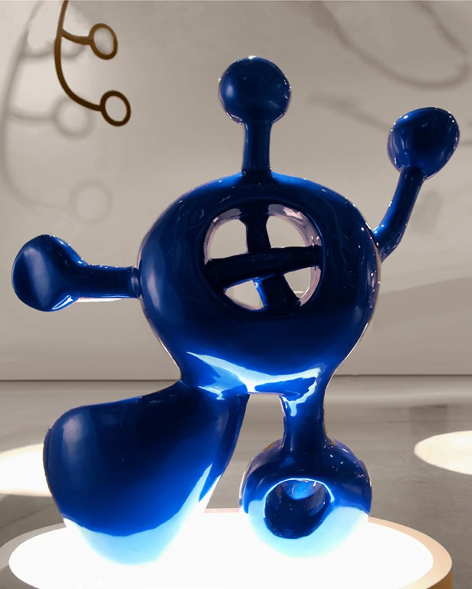 Blue abstract glass sculpture with multiple rounded projections, set on a round illuminated platform.