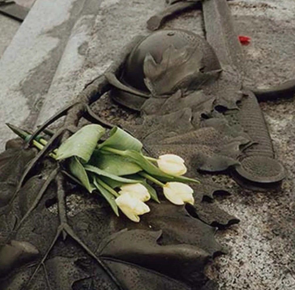A memorial with a helmet, a pair of shoes, and white flowers laid on a stone surface.