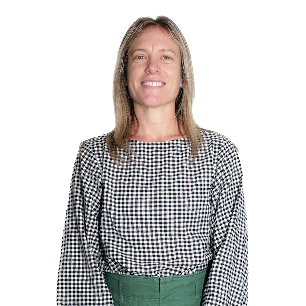 A woman with blonde hair smiling at the camera, wearing a black and white gingham long-sleeve shirt and green pants.