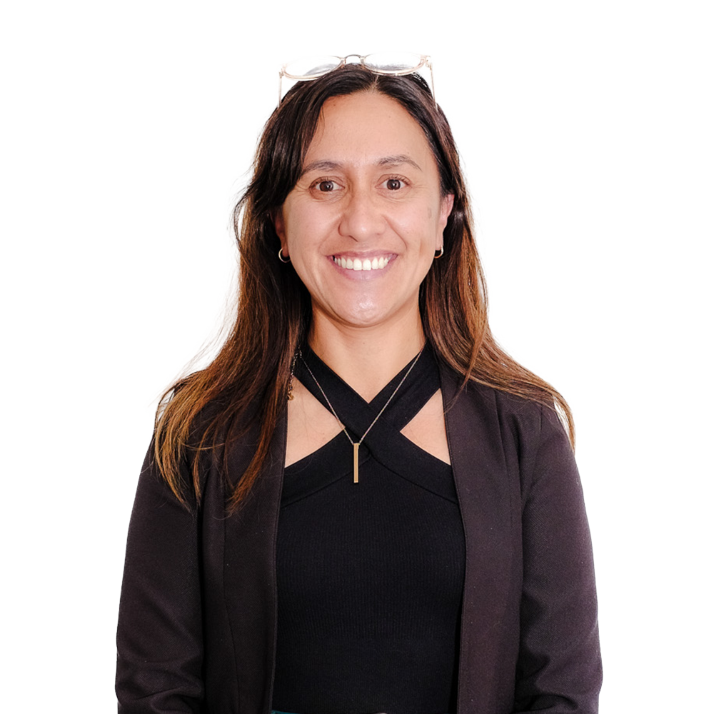 Smiling woman with glasses on her head, wearing a black top and black blazer, standing against a white background.