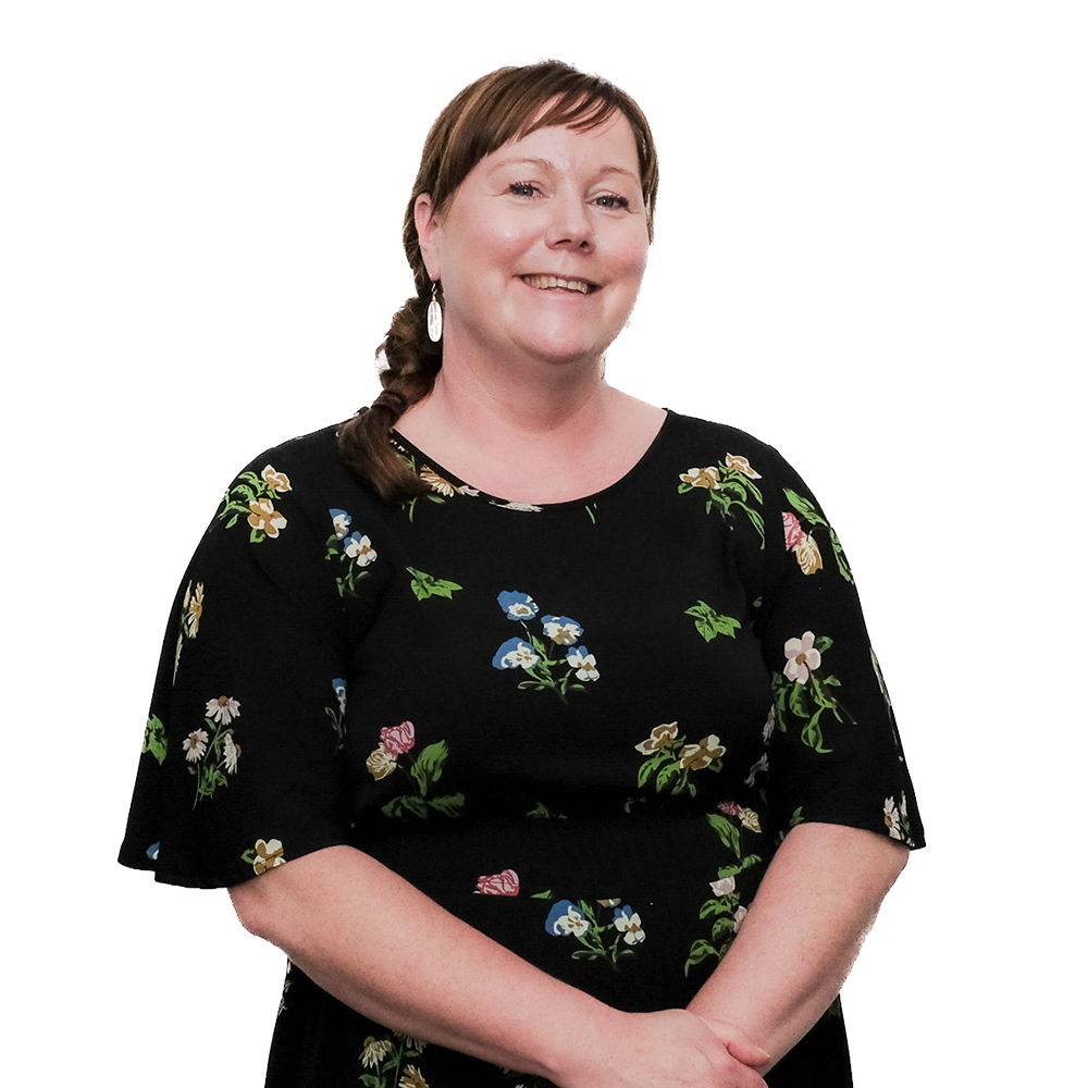 A woman with brown hair in a braid, wearing a black floral dress, smiling with arms crossed in front of a white background.