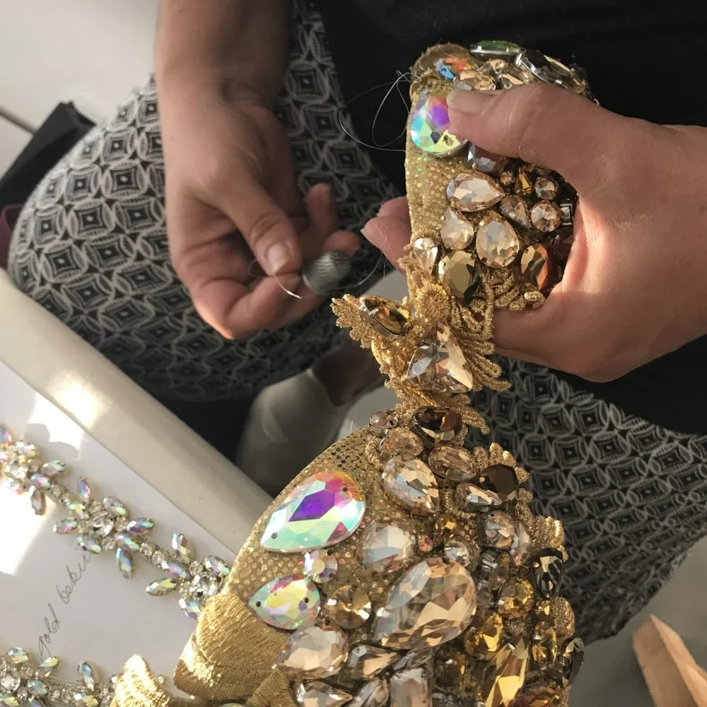 SambaCouture atelier -A person sewing a gold and crystal embellished headpiece with a needle and thread.