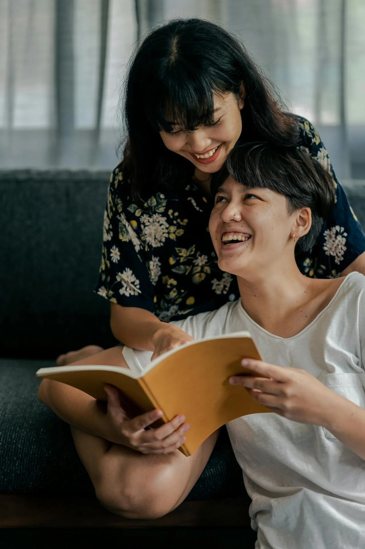 Two women sharing a joyful moment while reading a book together on a sofa.