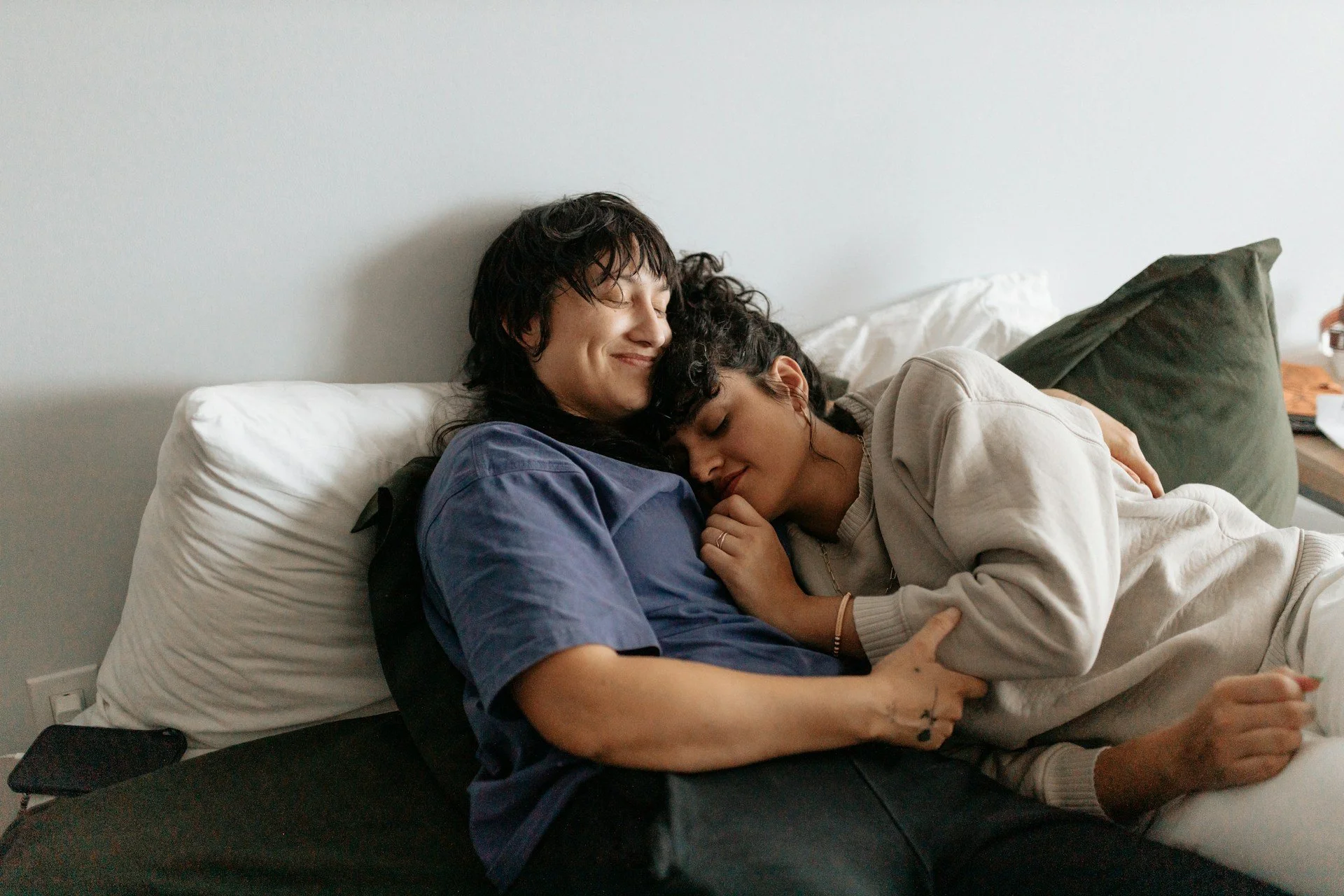 A couple cuddling peacefully on a bed, smiling and with their eyes closed.