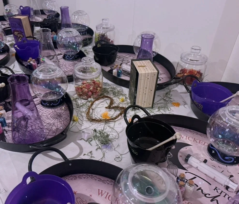 Table with Halloween-themed decorations including glass jars, purple pitchers, black bowls, and artificial spider webs.