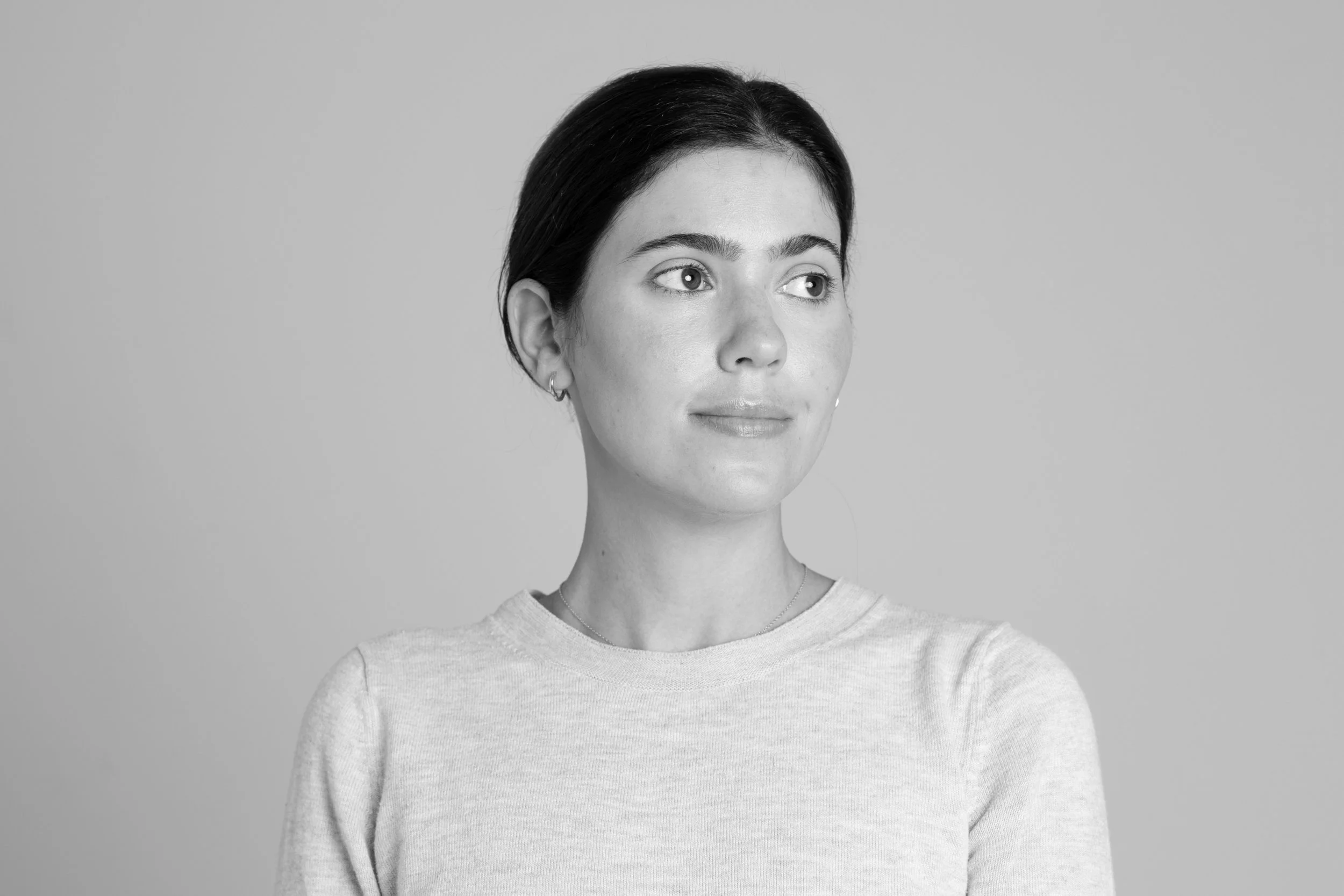 Black and white portrait of a woman with dark hair, wearing earrings and a light-colored shirt, looking to her right.
