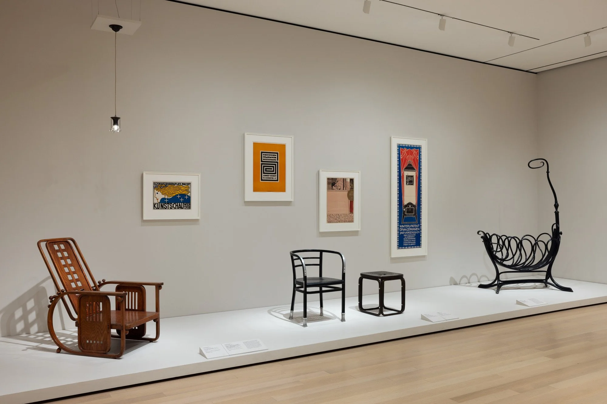 Exhibit of various modern and vintage chairs and framed artwork on a white gallery wall.