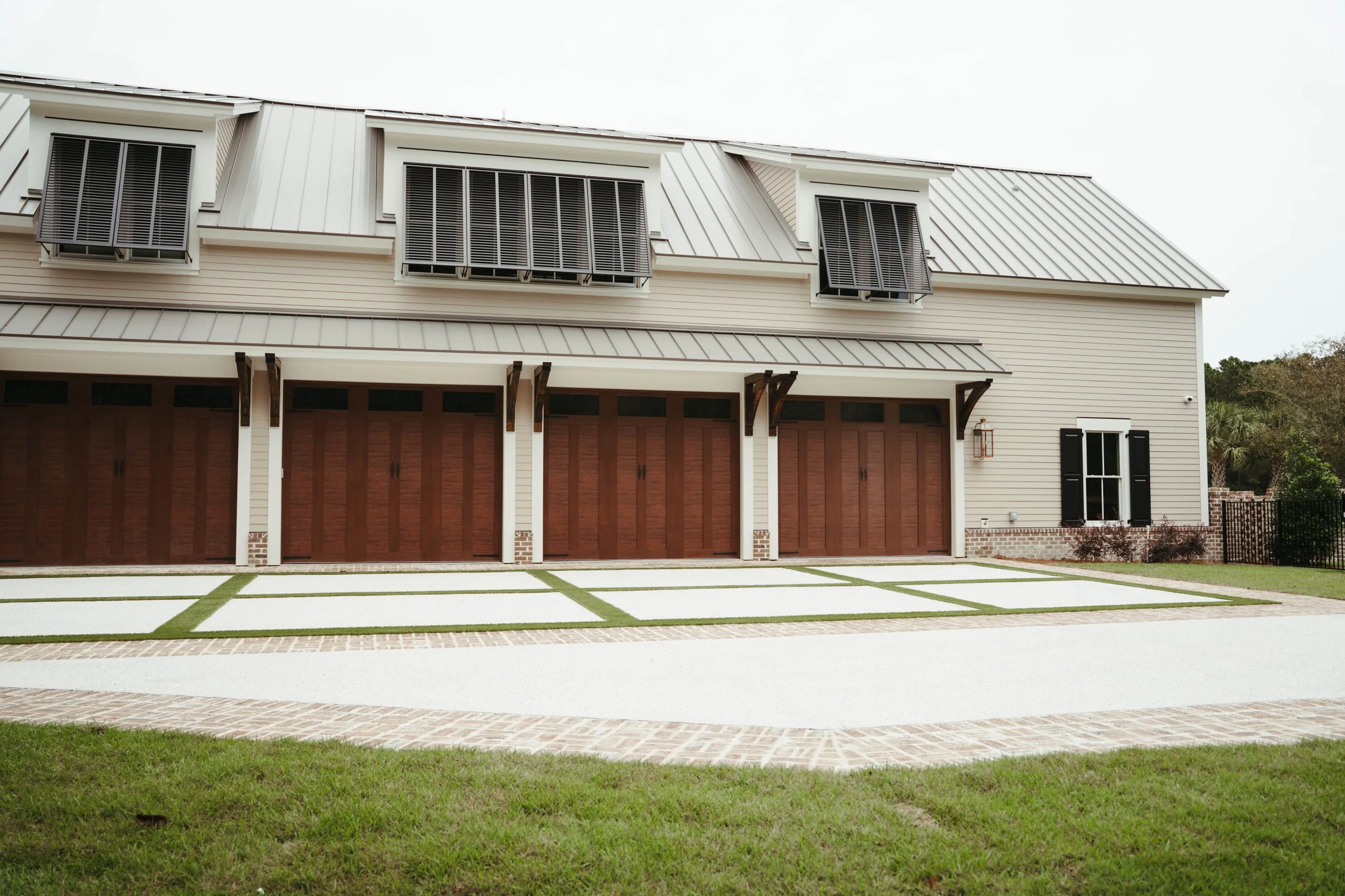 Front view of a modern, beige two-story house with four garage doors made of wood and a brick driveway.