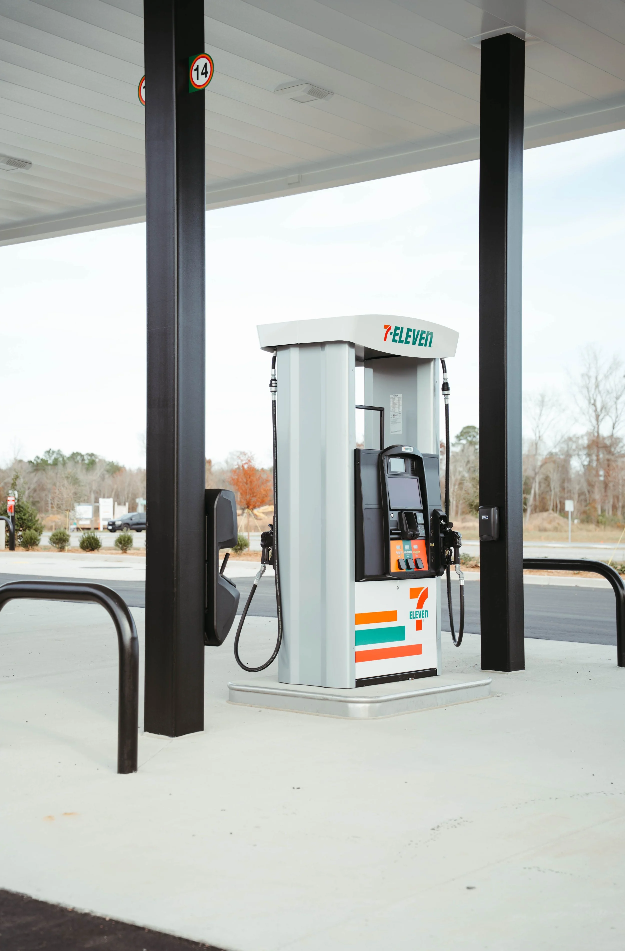 A 7-Eleven convenience store gas station pump with two fuel nozzles, digital display, and 7-Eleven branding, under a canopy on a cloudy day.