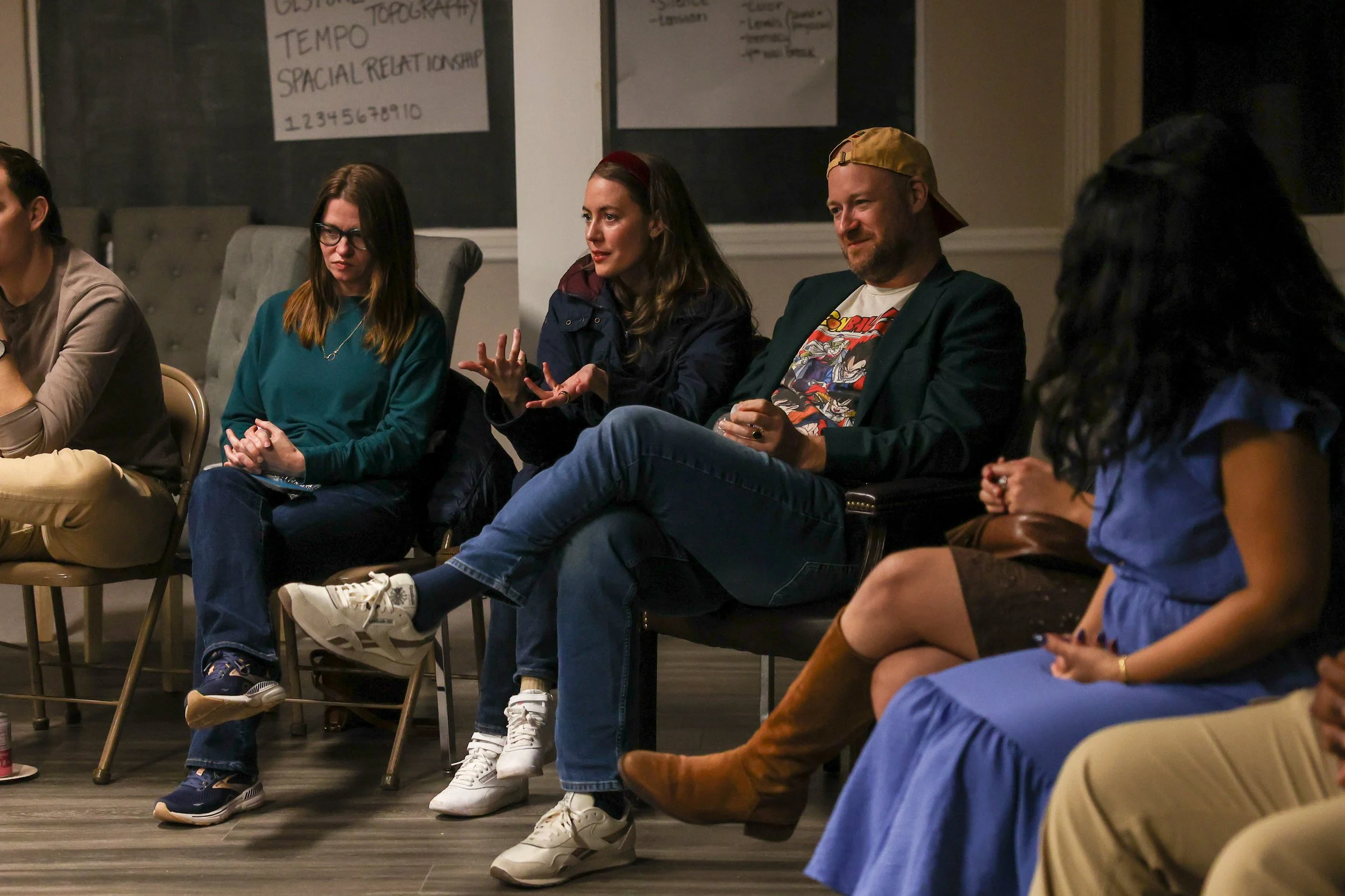 People sitting in chairs at the Mr Jesus community screening, engaged in a discussion in a room with blackboards or posters on the wall.